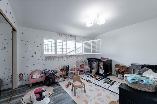 bedroom featuring vaulted ceiling, a closet, a crib, and hardwood / wood-style flooring