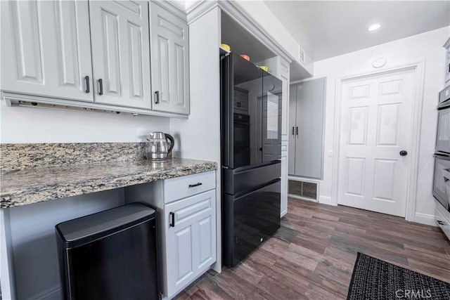 kitchen with white cabinetry, stone counters, dark hardwood / wood-style floors, oven, and built in desk