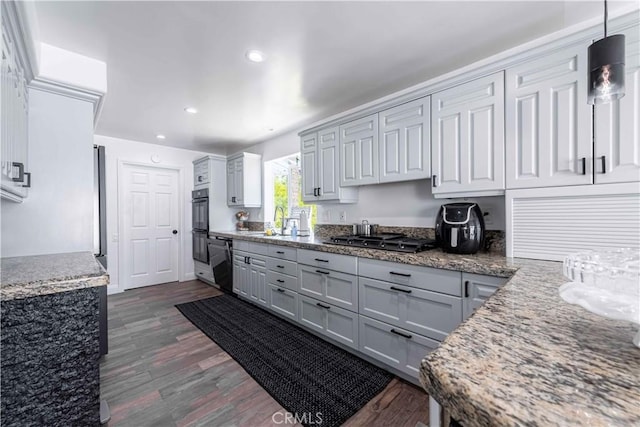 kitchen featuring dark wood-type flooring, sink, black appliances, stone countertops, and decorative light fixtures