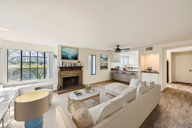 living room with ceiling fan, light hardwood / wood-style floors, and a stone fireplace