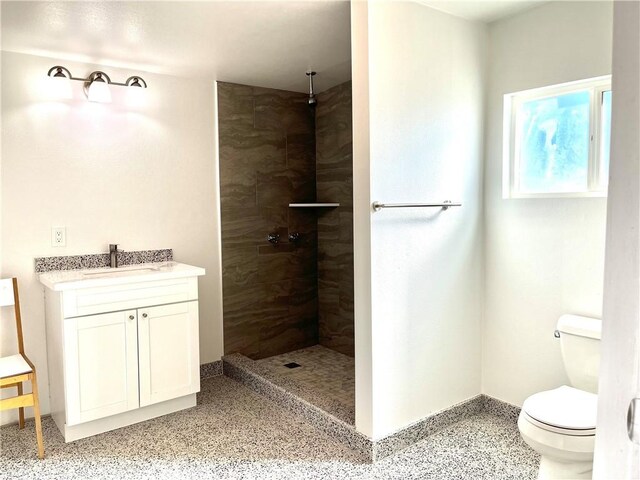 bathroom with a tile shower, vanity, and toilet