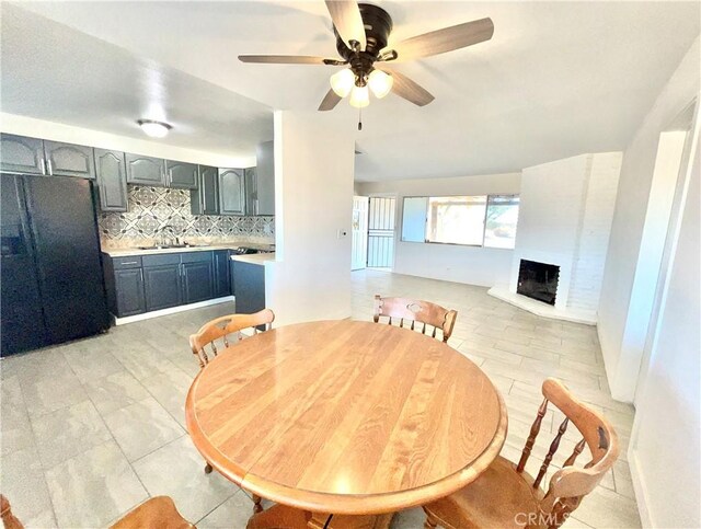 tiled dining room with ceiling fan, sink, and a brick fireplace