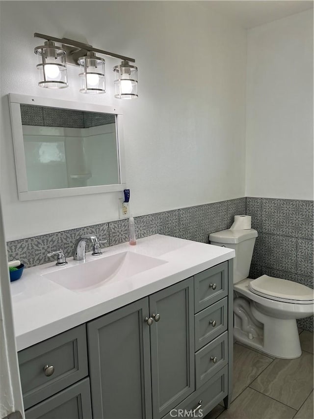 bathroom with vanity, toilet, and tile walls