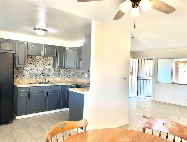 kitchen featuring decorative backsplash, black fridge, sink, and ceiling fan