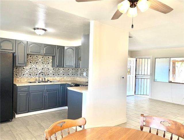 kitchen with sink, backsplash, light tile patterned floors, ceiling fan, and black fridge