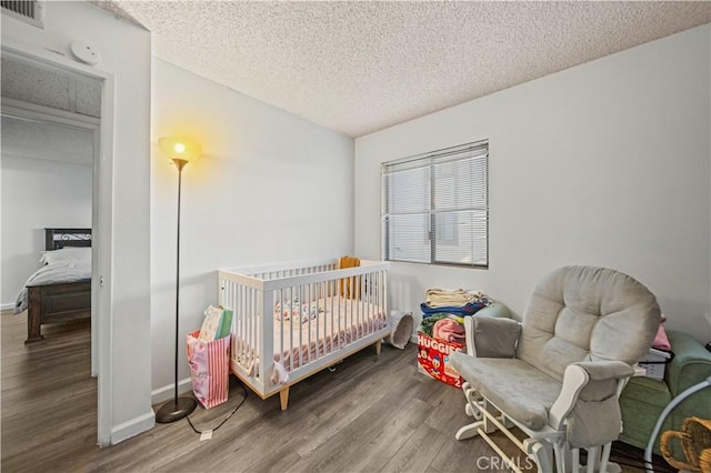 bedroom featuring a crib, hardwood / wood-style floors, and a textured ceiling