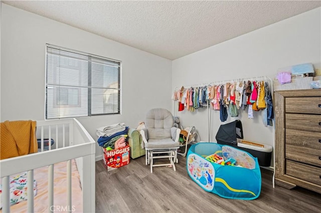 bedroom with a crib, wood-type flooring, and a textured ceiling