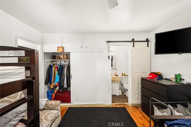 bedroom featuring ceiling fan, a barn door, connected bathroom, light hardwood / wood-style floors, and a closet