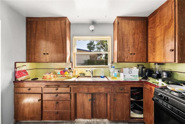 kitchen featuring black gas range oven, backsplash, tile countertops, and sink