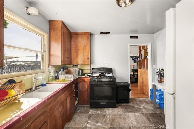 kitchen with tile countertops, sink, and black gas range oven