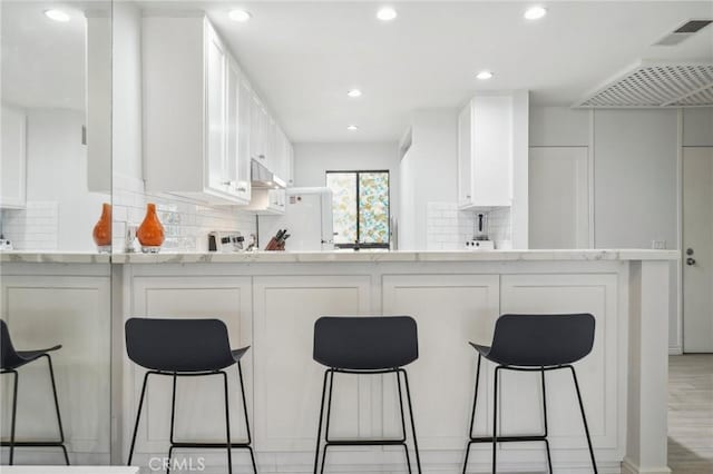 kitchen featuring white cabinets, decorative backsplash, and light stone countertops