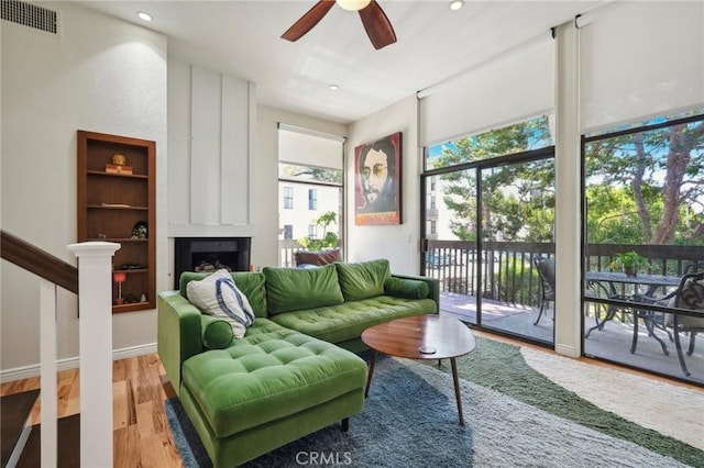 living room featuring ceiling fan, a large fireplace, and light hardwood / wood-style floors