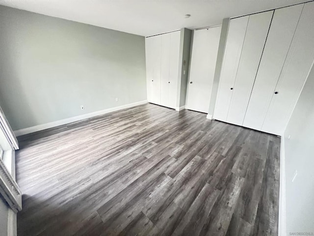 unfurnished bedroom featuring dark wood-type flooring and two closets