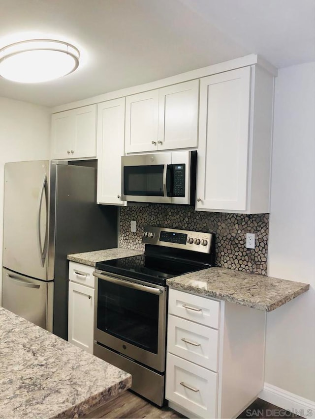 kitchen with light stone countertops, appliances with stainless steel finishes, white cabinetry, dark hardwood / wood-style flooring, and backsplash