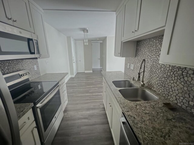 kitchen featuring hardwood / wood-style floors, appliances with stainless steel finishes, white cabinetry, dark stone countertops, and sink