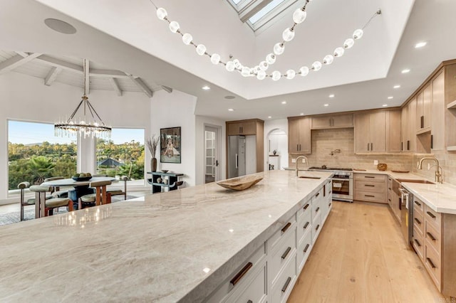 kitchen with light stone countertops, backsplash, lofted ceiling with skylight, light hardwood / wood-style floors, and light brown cabinetry