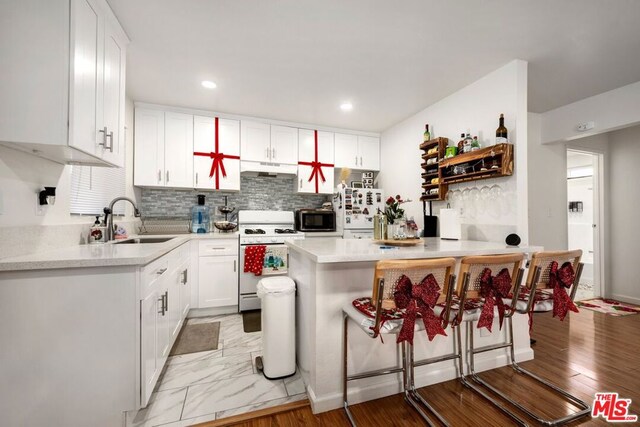 kitchen with white appliances, white cabinets, a kitchen breakfast bar, sink, and light hardwood / wood-style flooring