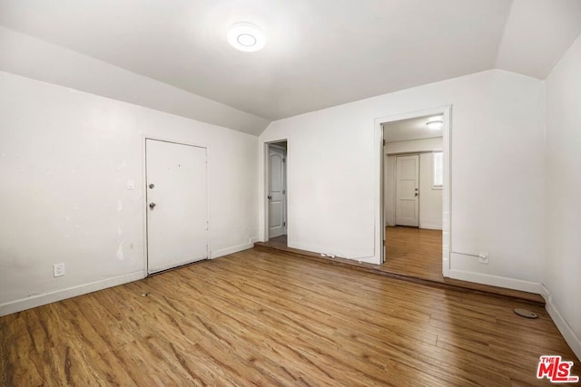 unfurnished bedroom with light wood-type flooring, vaulted ceiling, and a closet