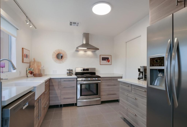 kitchen featuring sink, wall chimney exhaust hood, stainless steel appliances, rail lighting, and kitchen peninsula