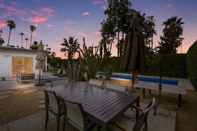 patio terrace at dusk featuring a fenced in pool