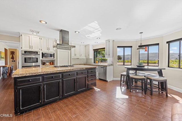 kitchen featuring appliances with stainless steel finishes, white cabinets, hanging light fixtures, island exhaust hood, and crown molding