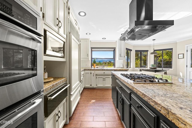 kitchen with hanging light fixtures, stainless steel appliances, island range hood, ornamental molding, and white cabinets