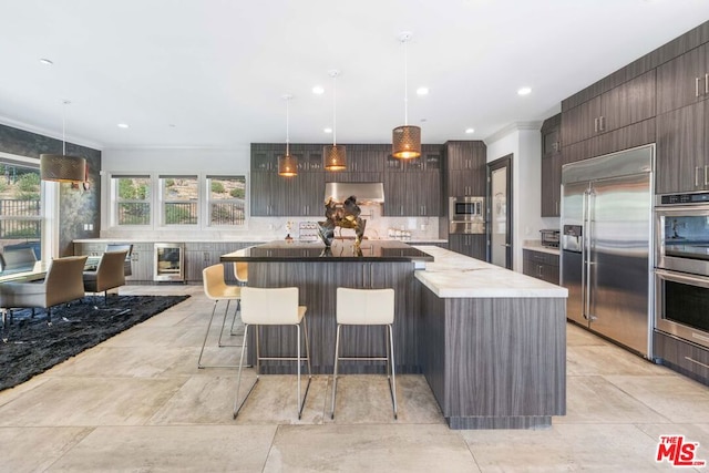 kitchen with a kitchen bar, backsplash, wall chimney range hood, pendant lighting, and built in appliances