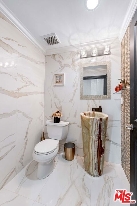 bathroom with crown molding, tile walls, and toilet