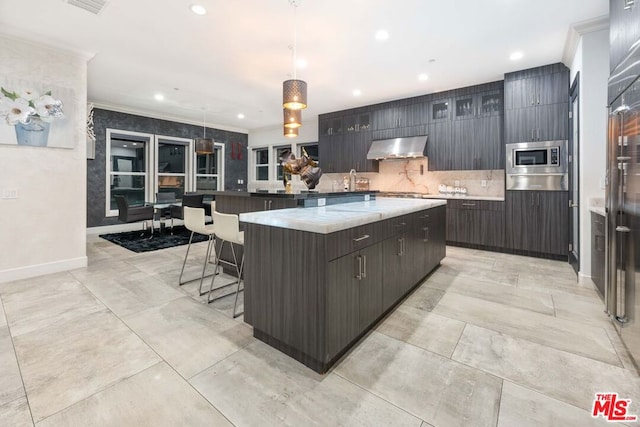 kitchen featuring ventilation hood, decorative light fixtures, a breakfast bar area, stainless steel microwave, and a large island