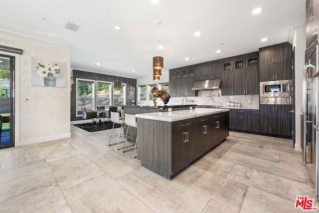 kitchen featuring stainless steel microwave, a center island, extractor fan, decorative light fixtures, and dark brown cabinets