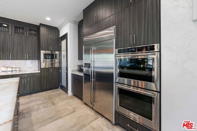 kitchen featuring built in appliances, dark brown cabinets, decorative backsplash, and crown molding