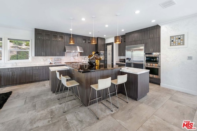 kitchen featuring appliances with stainless steel finishes, backsplash, exhaust hood, pendant lighting, and a large island