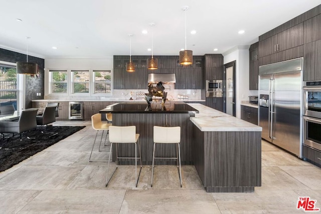 kitchen with pendant lighting, backsplash, exhaust hood, built in appliances, and beverage cooler