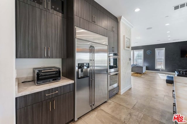 kitchen featuring appliances with stainless steel finishes, dark brown cabinets, and ornamental molding