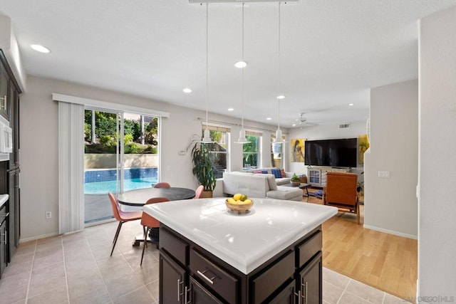 kitchen with dark brown cabinets, pendant lighting, ceiling fan, light tile patterned floors, and a kitchen island