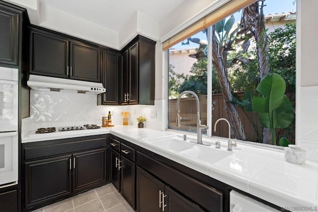 kitchen with white appliances, dark brown cabinetry, tasteful backsplash, sink, and light tile patterned floors