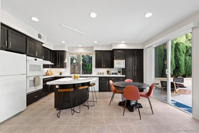 kitchen with white appliances, hanging light fixtures, light tile patterned floors, a kitchen island, and a breakfast bar area