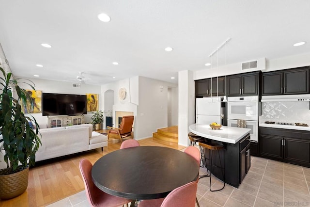 kitchen with white appliances, a center island, decorative backsplash, ceiling fan, and a breakfast bar area