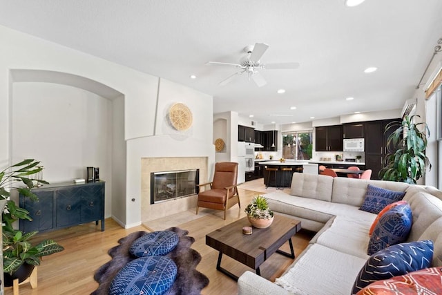 living room with ceiling fan, a tile fireplace, and light hardwood / wood-style floors