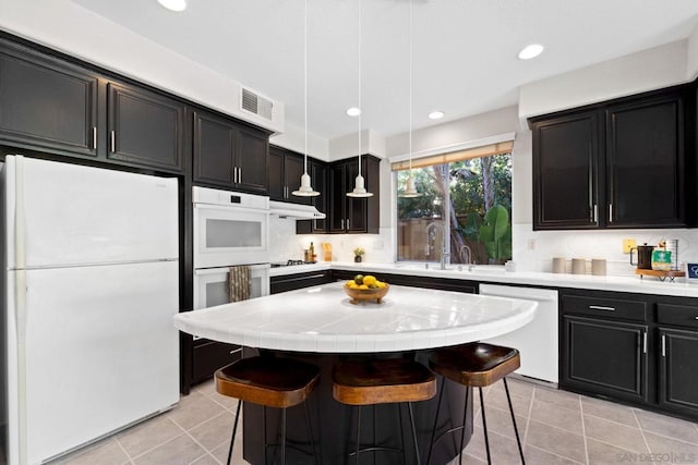 kitchen featuring a center island, white appliances, a kitchen breakfast bar, pendant lighting, and light tile patterned flooring