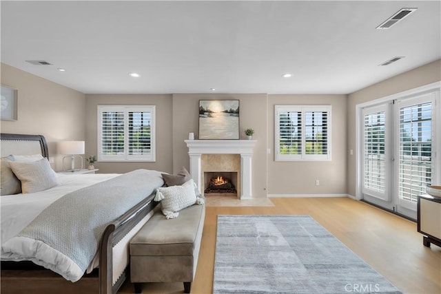 bedroom featuring a fireplace, access to exterior, multiple windows, and light hardwood / wood-style flooring