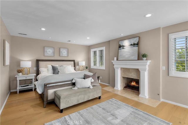 bedroom with multiple windows, a fireplace, and light hardwood / wood-style flooring