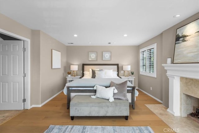 bedroom with a high end fireplace and light hardwood / wood-style flooring