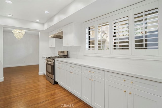 kitchen featuring ventilation hood, white cabinets, gas range, light wood-type flooring, and a chandelier