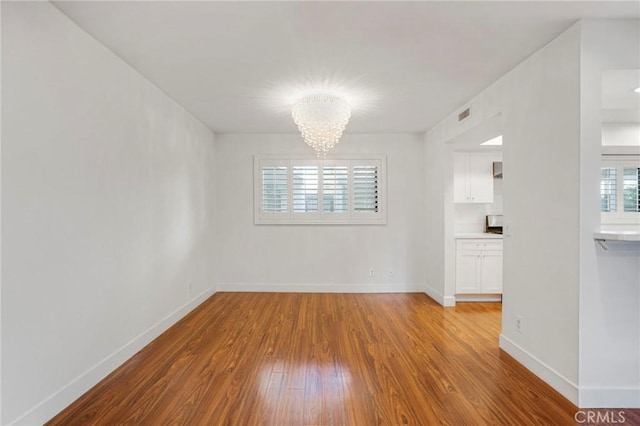 empty room with a notable chandelier and light wood-type flooring