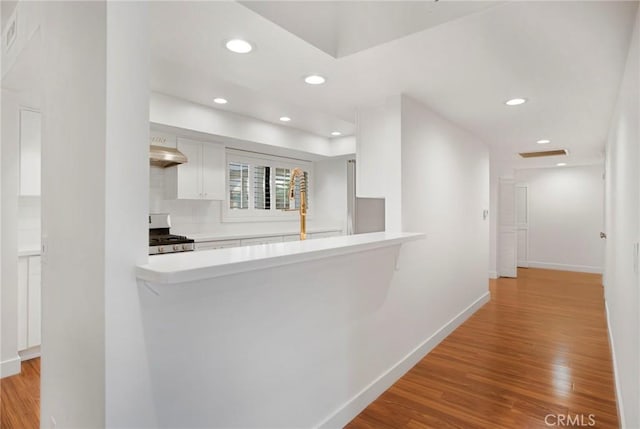 kitchen featuring kitchen peninsula, light wood-type flooring, gas range, extractor fan, and white cabinetry