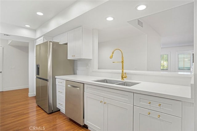 kitchen with white cabinetry, sink, stainless steel appliances, light hardwood / wood-style flooring, and kitchen peninsula