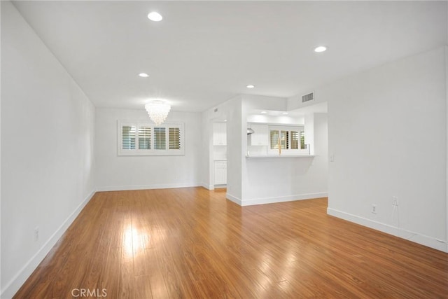 unfurnished living room featuring a chandelier, light wood-type flooring, and plenty of natural light