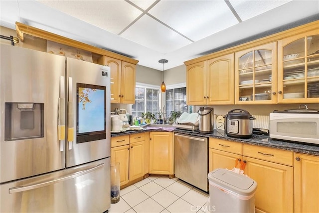 kitchen featuring light brown cabinets, stainless steel appliances, dark stone countertops, decorative light fixtures, and light tile patterned floors