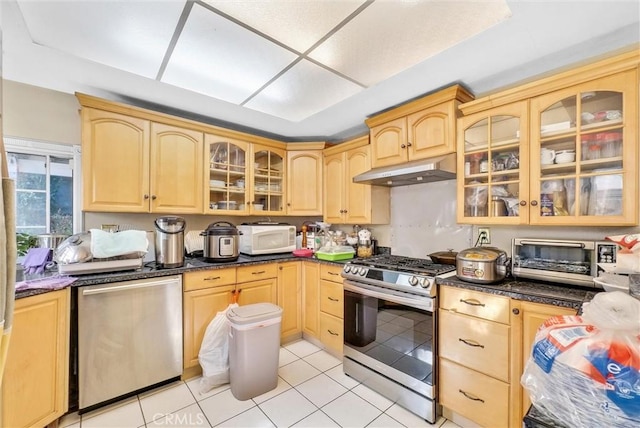 kitchen featuring dark stone countertops, light brown cabinets, light tile patterned floors, and appliances with stainless steel finishes